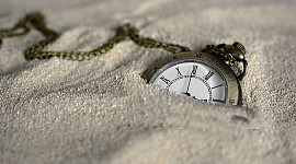 एक पॉकेट घड़ी रेत में आधी दबी हुई है