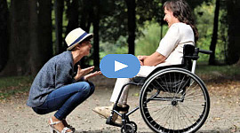 pessoa carinhosa de cócoras na frente de outra em uma cadeira de rodas