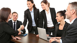נשים לוחצות ידיים בפגישה עסקית, עם גברים מסתכלים