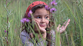 niña en un campo de pastos altos y flores silvestres