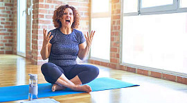 kobieta siedząca na macie do jogi z rękami uniesionymi do góry, sfrustrowana i krzycząca