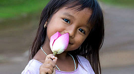 glimlaggende jong meisie wat 'n onoopgemaakte lotusblom vashou