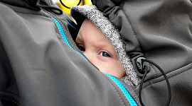 एक बच्चा अपनी माँ की जैकेट के अंदर उसकी छाती पर छिपा हुआ है