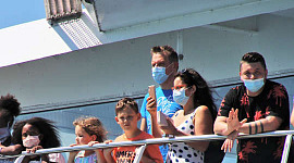 pessoas, a maioria usando máscaras, em pé no parapeito de um navio de cruzeiro