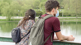 pasangan muda, memakai topeng pelindung, berdiri di atas jambatan