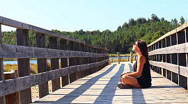 mujer joven frente al sol y sentada en un puente de madera