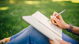 一个人坐在外面的草地上，在笔记本上写字