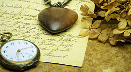 um relógio de bolso e um pingente de coração em cima de uma carta manuscrita