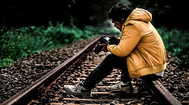 joven sentado en las vías del tren mirando las fotos en su cámara