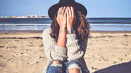 年轻女子坐在沙滩上，脸藏在带子里