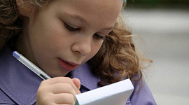 egy fiatal lány, aki elszántan ír egy papírtömbre