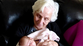egy nagymama (vagy talán egy dédnagymama), aki egy újszülött gyermeket tart a kezében