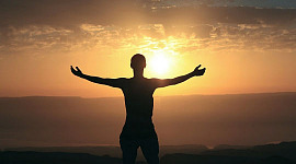 uma pessoa com os braços abertos de frente para o sol nascente