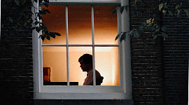 человек, сидящий один в доме, увиденный через окно