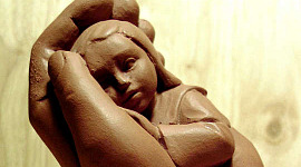 gliniana rzeźba przedstawiająca dziecko trzymane w wspierającej dłoni