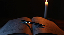 en åben bog med en kuglepen liggende på og et lys skinner på bogen