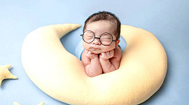 gözleri kapalı, kocaman gözlükler takmış ve hilal şeklinde bir yastık üzerinde dinlenen bebek