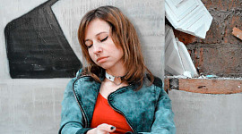 یک زن جوان با ظاهری مأیوس که کنار دیوار نشسته است
