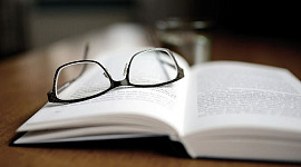 sebuah buku terbuka dengan sepasang kacamata tergeletak di atasnya