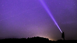 seorang kanak-kanak memancarkan lampu suluh ke langit berbintang pada waktu malam
