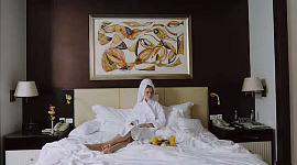 en person som sitter uppe på en hotellsäng och äter frukost på sängen