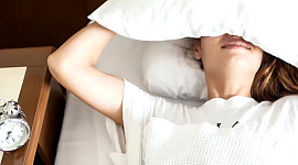 頭の上に枕を置き、ベッドの横に目覚まし時計を置いてベッドに横たわっている人