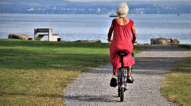 a senior woman with white hair and a red dress riding a bicycle