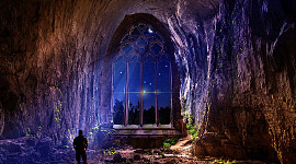 en mann i en hule med en enorm bue som åpner seg mot natt og himmel