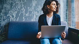 nainen istuu kannettavan tietokoneen edessä katsoen kaukaisuuteen
