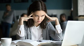 молодая женщина смотрит на свой ноутбук и прижимает искатели к голове