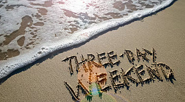 रेत में लिखे "3-दिवसीय सप्ताहांत" शब्दों वाला एक समुद्र तट