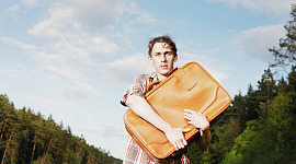 mężczyzna stojący na zewnątrz, przyciskając walizkę do piersi