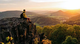 en vandrer, der sidder på et fremspring af klipper ude i naturen