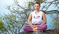 Mujer joven sentada afuera en una posición de meditación.