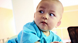 一個穿著藍色襯衫的嬰兒睜大眼睛看著他的肩膀