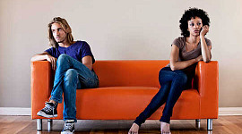 Um casal está sentado em lados opostos de um sofá laranja olhando para longe um do outro