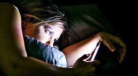 بستر پر ایک عورت اپنا فون پڑھ رہی ہے