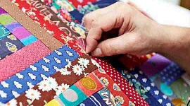 A person sews a quilt from many different pieces of fabric