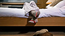 A person's legs hang over the side of their bed
