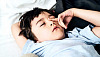 Młody chłopak przeciera oko, gdy leży w łóżku