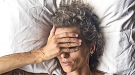 Una donna sdraiata su un cuscino bianco si mette una mano sul viso
