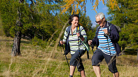 Una pareja mayor usa bastones de trekking mientras camina.